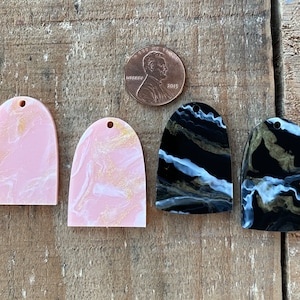 May include: Four resin arch-shaped charms with marbled patterns. Two are pink with gold flecks, and two are black with white and gold flecks.