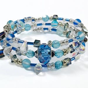 May include: A multi-strand bracelet with blue, clear, and iridescent beads. The bracelet features a large, faceted, dark blue crystal bead in the center.