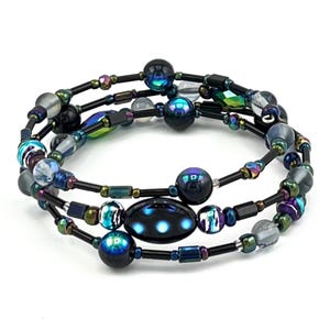 May include: A triple-wrap bracelet with black, blue, and iridescent beads. The bracelet features a large, oval-shaped bead with a black background and white polka dots.