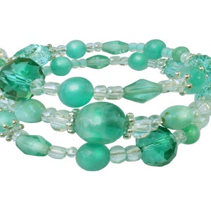 May include: A multi-strand bracelet with green and clear beads. The beads are round, faceted, and irregular, strung on a flexible wire. The bracelet wraps around the wrist. The beads are in various shades of green.