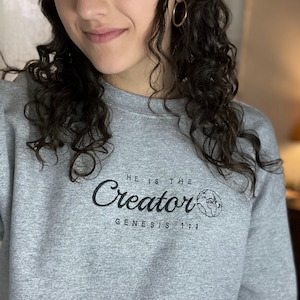 May include: A gray sweatshirt with a black graphic that says "He is the Creator Genesis 1:1" with a small image of the Earth.