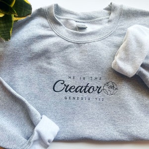 May include: A gray sweatshirt with the text "He is the Creator Genesis 1:1" and a small graphic of the Earth.