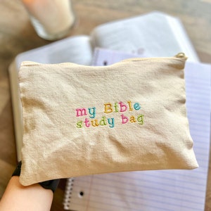 May include: A beige canvas bag with a zipper closure. The bag has colorful embroidery that reads "my Bible study bag".