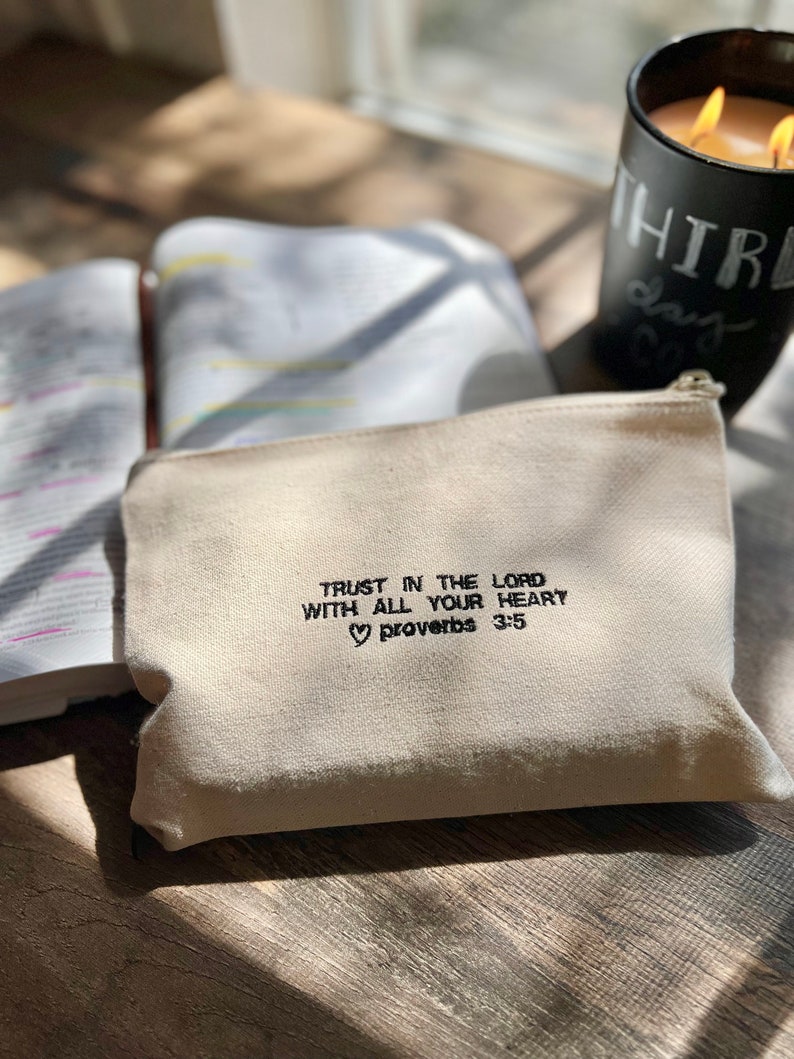 Peut inclure: Une pochette zipp&eacute;e en toile blanche avec le texte "Trust in the Lord with all your heart Proverbs 3:5" brod&eacute; en noir.
