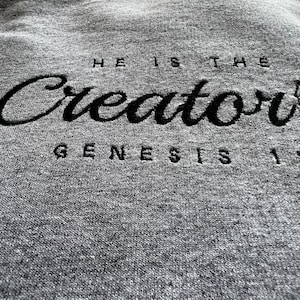 May include: Gray hooded sweatshirt with black embroidered text that reads "He is the Creator Genesis 1".