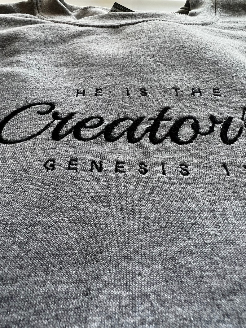 May include: Gray hooded sweatshirt with black embroidered text that reads "He is the Creator Genesis 1".