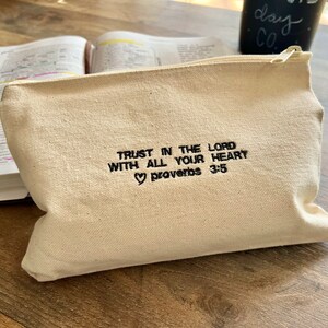 Peut inclure: Une pochette zipp&eacute;e en toile beige avec le texte "Trust in the Lord with all your heart Proverbs 3:5" brod&eacute; en noir.