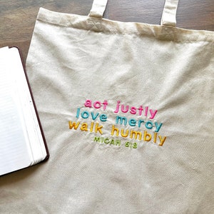 May include: A beige canvas tote bag with the words "act justly, love mercy, walk humbly, Micah 6:8" embroidered in colorful letters.