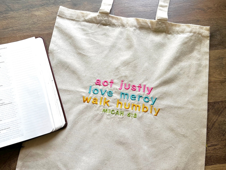 May include: A beige canvas tote bag with the words "act justly, love mercy, walk humbly, Micah 6:8" embroidered in colorful letters.