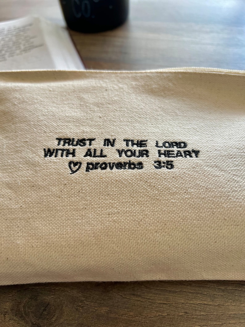 Peut inclure: Une pochette zipp&eacute;e en toile blanche avec un texte brod&eacute; en noir qui dit "TRUST IN THE LORD WITH ALL YOUR HEART &hearts; Proverbs 3:5".