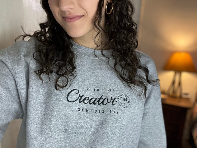 May include: A gray sweatshirt with a black graphic that says "He is the Creator Genesis 1:1" with a small image of the Earth.