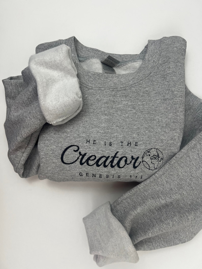 May include: Gray sweatshirt with a black graphic that says "He is the Creator Genesis 1:1" with a small globe image.