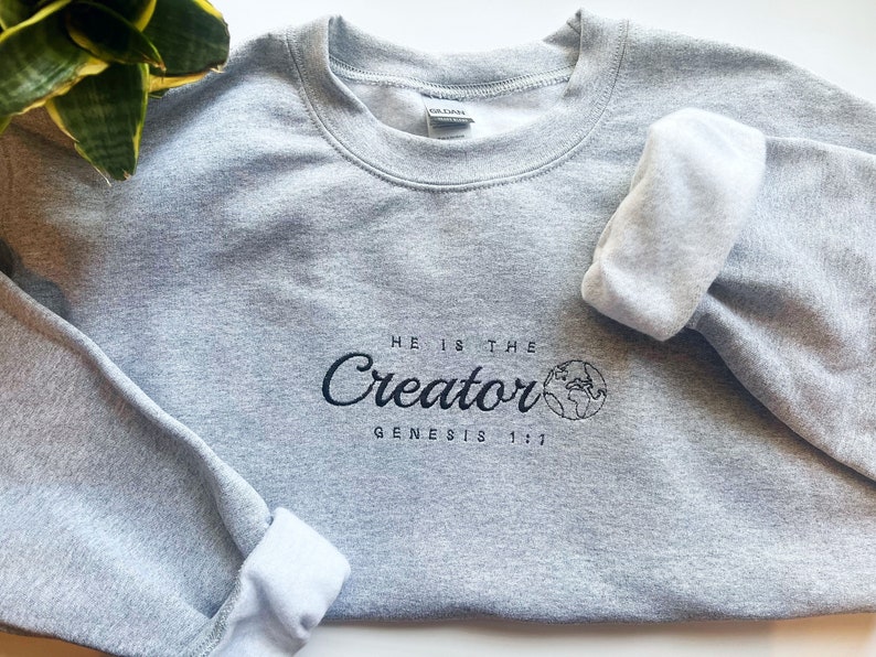 May include: A gray sweatshirt with the text "He is the Creator Genesis 1:1" and a small graphic of the Earth.