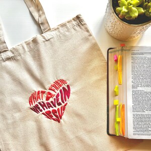 Op de afbeelding: Een witte canvas tote bag met een rood en roze geborduurd hart waarop staat "Wat een vriend hebben we in Jezus".