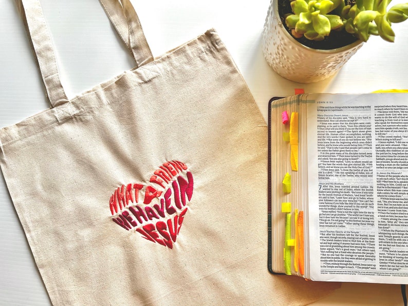 Op de afbeelding: Een witte canvas tote bag met een rood en roze geborduurd hart waarop staat "Wat een vriend hebben we in Jezus".