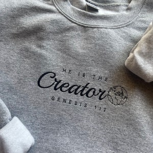 May include: Gray sweatshirt with black embroidered text that reads "HE IS THE Creator GENESIS 1:1" with a small embroidered image of the Earth.