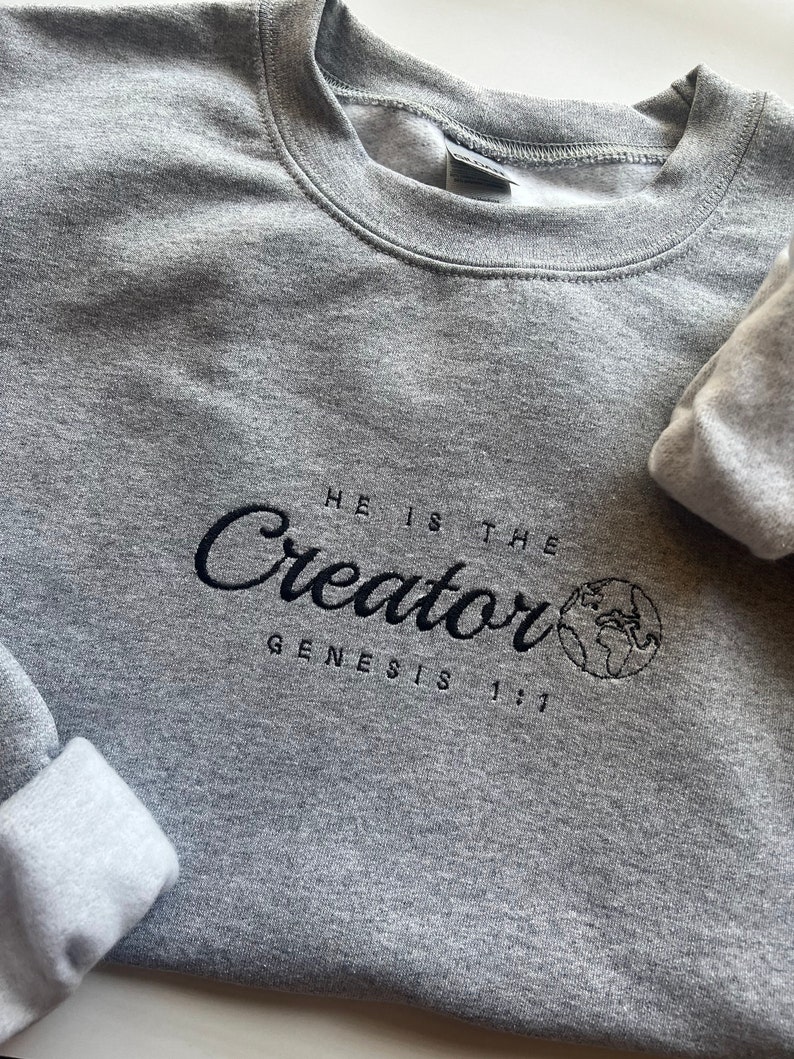 May include: Gray sweatshirt with black embroidered text that reads "HE IS THE Creator GENESIS 1:1" with a small embroidered image of the Earth.