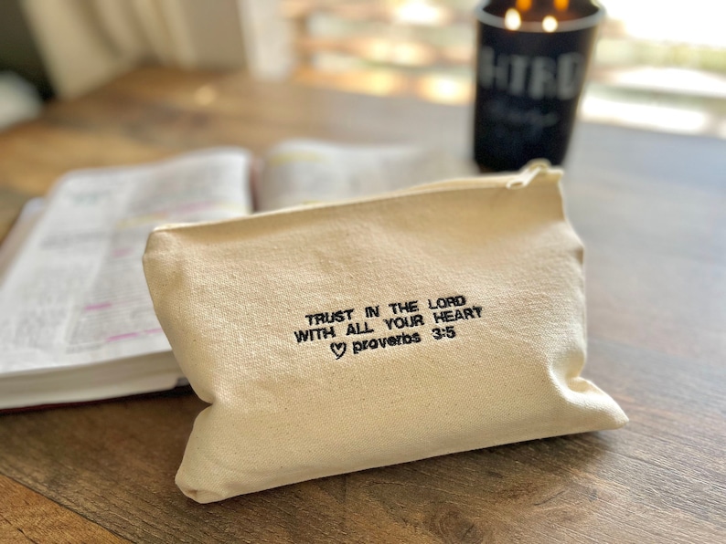 Peut inclure: Une pochette zipp&eacute;e en toile beige avec le texte "Trust in the Lord with all your heart &hearts; Proverbs 3:5" brod&eacute; en noir.