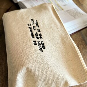 Peut inclure: Une pochette zipp&eacute;e en toile blanche avec une broderie noire qui dit "Fais confiance au Seigneur de tout ton c&oelig;ur" Proverbes 3:5.