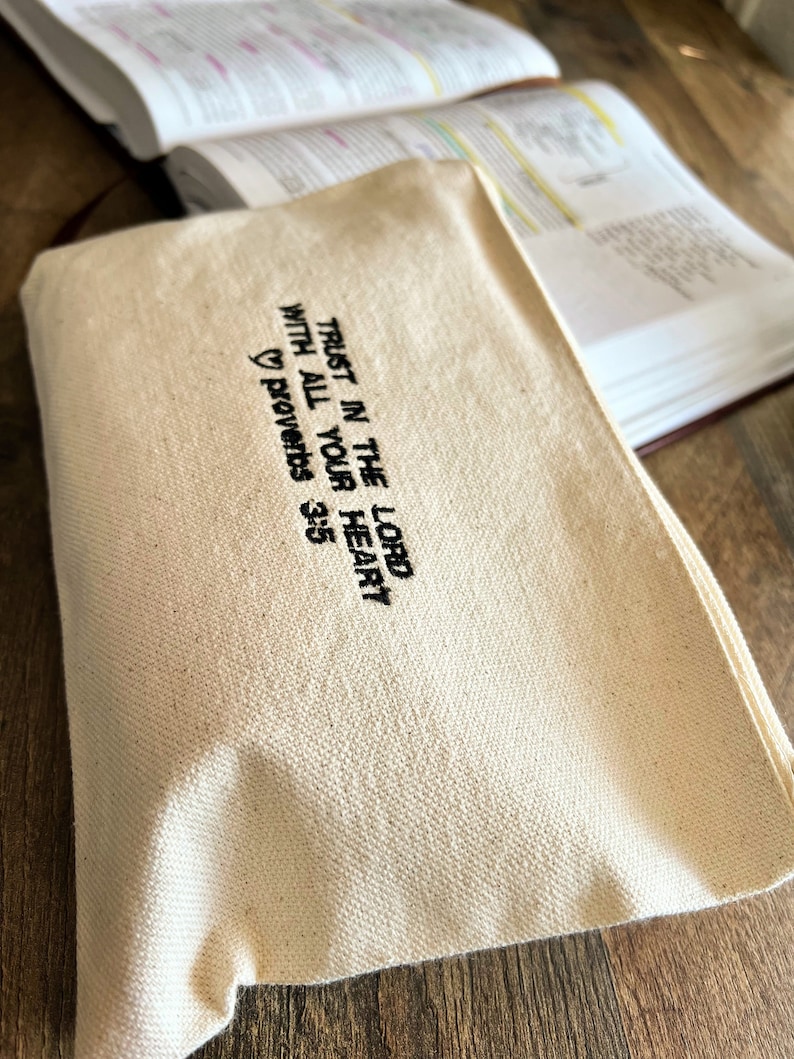 Peut inclure: Une pochette zipp&eacute;e en toile blanche avec une broderie noire qui dit "Fais confiance au Seigneur de tout ton c&oelig;ur" Proverbes 3:5.
