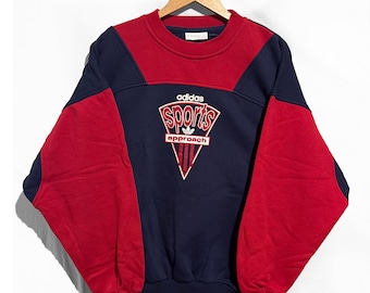 May include: A vintage Adidas Sports Approach sweatshirt. The sweatshirt is navy blue with red accents on the shoulders and sleeves. The Adidas logo and "Sports Approach" text are in white and red.