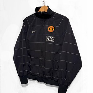 K&ouml;nnte beinhalten: Eine wei&szlig;e Keramik-Tasse mit schwarzem Henkel und dem Text "But First, Coffee" in schwarzer, handschriftlicher Schrift. Die Tasse steht auf einer wei&szlig;en Oberfl&auml;che.