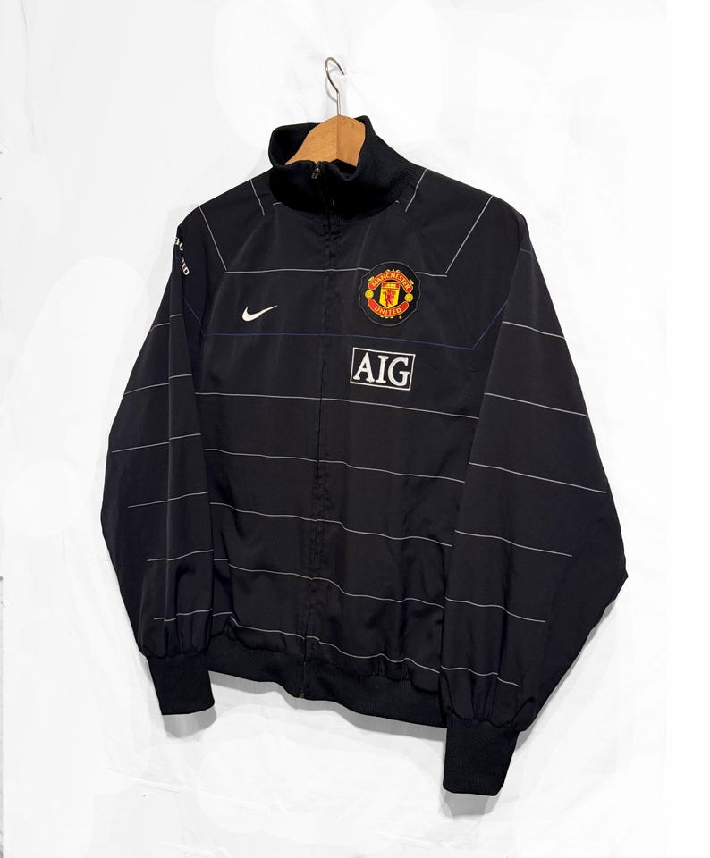 K&ouml;nnte beinhalten: Eine wei&szlig;e Keramik-Tasse mit schwarzem Henkel und dem Text "But First, Coffee" in schwarzer, handschriftlicher Schrift. Die Tasse steht auf einer wei&szlig;en Oberfl&auml;che.