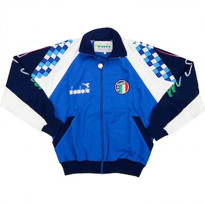 Könnte beinhalten: Blau-weiß-marinefarbene Trainingsjacke mit durchgehendem Reißverschluss. Die Jacke zeigt die italienische Flagge, ein Schachbrettmuster auf den Ärmeln und das "diadora"-Logo. Sie hat einen Stehkragen und zwei Vordertaschen.
