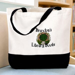 Pode incluir: Uma sacola de lona branca com painel inferior preto e alças pretas. A frente apresenta um gráfico de uma porta redonda verde em um arco de pedra cercado por vegetação, com o texto Braxton's Library Books impresso em preto.