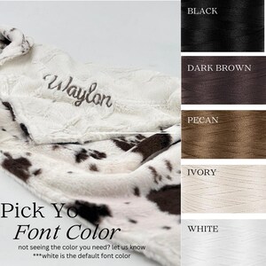 May include: A plush, cow-print blanket with the name "Waylon" embroidered in a script font. The image includes a color chart with thread options: black, dark brown, pecan, ivory, and white. Text reads "Pick Your Font Color".