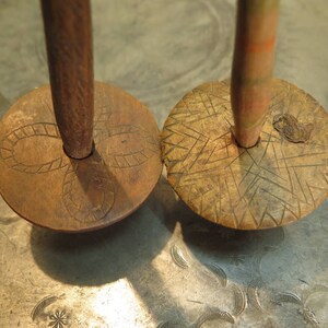 Könnte beinhalten: Zwei Holz-Kreisel mit geschnitzten Designs. Die Kreisel sind braun und haben eine Spindel in der Mitte. Die Spindel ist aus Holz und mit roten und weißen Streifen bemalt.