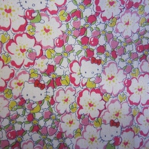 May include: A white fabric with a repeating pattern of pink flowers, green leaves, red cherries, and cartoon Hello Kitty characters. The Hello Kitty characters are wearing red bows and holding strawberries.
