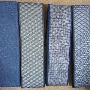 以下が含まれることがあります： 青とグレーの色合いの装飾用リボンの4つのロール。各リボンは、ダイヤモンド、ジグザグ、インターロッキングシェイプなど、ユニークな幾何学模様を特徴としています。リボンはしっかりと巻かれており、詳細な織り模様が示されています。