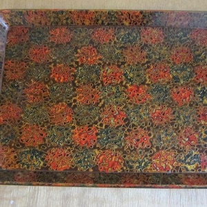 May include: Rectangular serving tray with a glossy finish. The tray features a repeating pattern of abstract floral shapes in shades of red, orange, yellow, green, and black against a brown background. The tray has rounded corners.