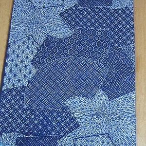 以下が含まれることがあります： 白い幾何学模様の青い布。布は円、正方形、星など、さまざまな形とデザインで構成されています。布は伝統的な日本のデザインです。