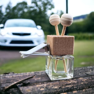 A stylish wooden and glass vent diffuser resting on a wooden surface, with a blurred car in the background. Designed for easy car vent attachment.