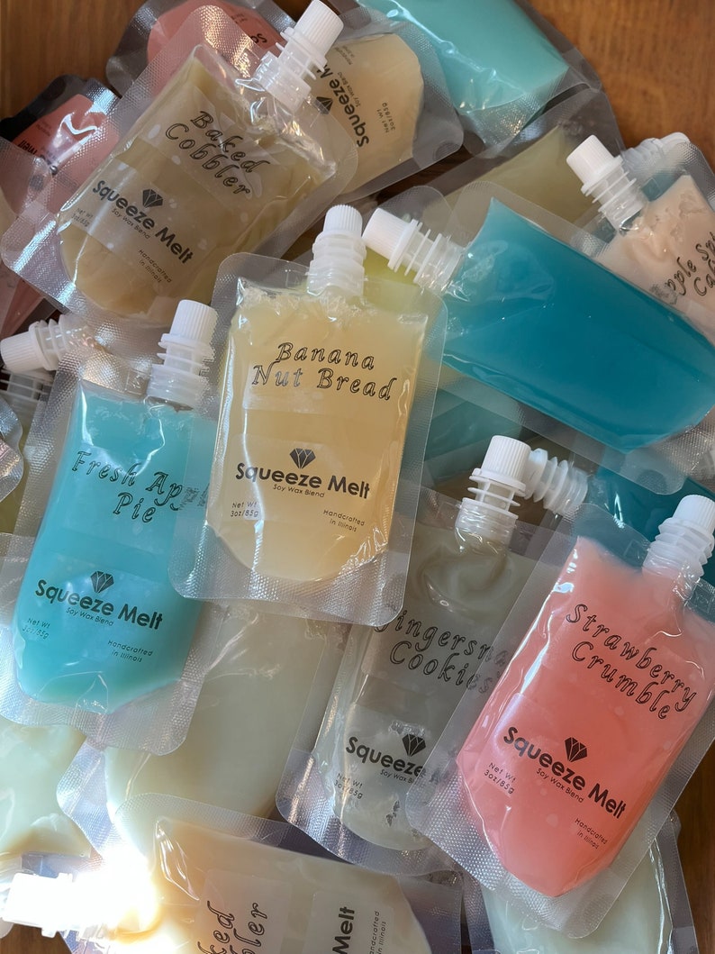 Puede incluir: Una variedad de bolsas coloridas con diferentes sabores de cera de soja derretida. Las bolsas est&aacute;n etiquetadas con nombres como "Baked Cobbler", "Banana Nut Bread", "Fresh Apple Pie", "Ginger Snap Cookies", "Strawberry Crumble" y "Squeeze Melt".