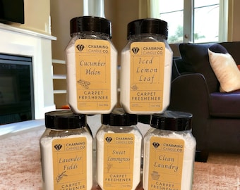 May include: Six glass jars with white powder inside. Each jar has a black lid and a brown label with the text "Charming Candle Co." and a different scent: Cucumber Melon, Iced Lemon Loaf, Lavender Fields, Sweet Lemongrass, Clean Laundry. Each jar is labeled "Carpet Freshener".