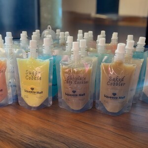 Puede incluir: Una variedad de bolsas coloridas llenas de diferentes sabores de pur&eacute; de frutas "Squeeze Melt". Los sabores incluyen Apple Spice Cake, Sugar Cookie, Chocolate Chip Cookies y Baked Cobbler.