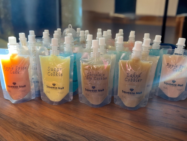Puede incluir: Una variedad de bolsas coloridas llenas de diferentes sabores de pur&eacute; de frutas "Squeeze Melt". Los sabores incluyen Apple Spice Cake, Sugar Cookie, Chocolate Chip Cookies y Baked Cobbler.