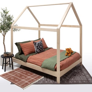 May include: A light-colored wooden house-shaped bed frame with a mattress featuring olive green and terracotta striped bedding. The bed includes a small plush leopard toy, a black and white patterned pillow, and a dark green throw blanket.