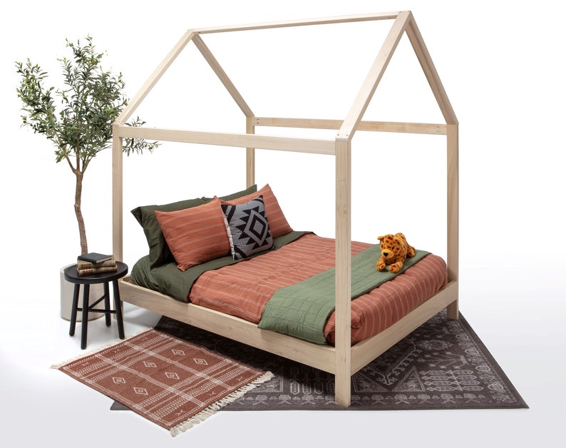 May include: A light-colored wooden house-shaped bed frame with a mattress featuring olive green and terracotta striped bedding. The bed includes a small plush leopard toy, a black and white patterned pillow, and a dark green throw blanket.