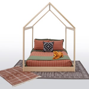 May include: A light-colored wooden house-shaped bed frame featuring a mattress with rust-colored striped bedding, olive green accents, a small square patterned throw pillow, and a plush leopard toy, placed on a dark patterned rug.