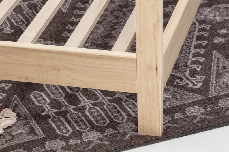 May include: A light-colored natural wood bed frame featuring a sturdy corner post and horizontal side rails. The structure includes a series of evenly spaced wooden slats designed to support a mattress, showcasing the grain of the unfinished wood.