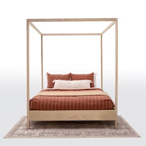 May include: A wooden canopy bed frame with a rust-colored striped bedspread and white and rust-colored pillows. The bed is sitting on a beige rug with a geometric pattern.