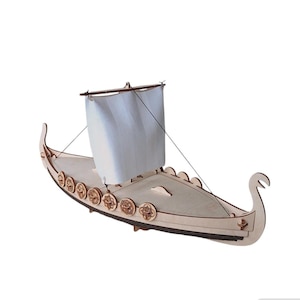 Könnte beinhalten: Ein Holzmodell eines Wikingerschiffs mit einem weißen Segel. Das Schiff hat einen geschnitzten Holzbug und eine Reihe von dekorativen Schilden an der Seite.