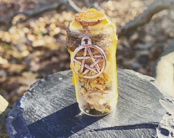 May include: A small glass bottle filled with crystals and sealed with wax. A silver pentagram charm hangs from the bottle's neck.