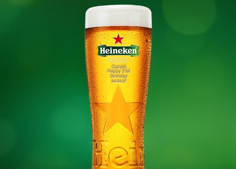 May include: A tall glass of Heineken beer, with condensation and a white foamy head. The glass has a star design and the Heineken logo. Text on the glass reads: "Gareth Happy 21st Birthday 24-04-27". The background is a solid green.