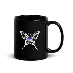 May include: Black ceramic coffee mug with a white butterfly design. The butterfly has a purple and white center.
