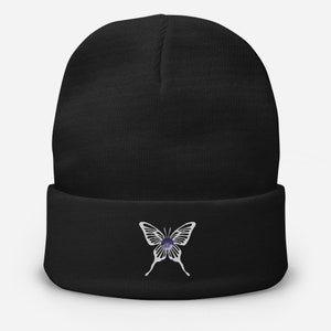 May include: Black beanie with a white butterfly design featuring a purple gemstone in the center.